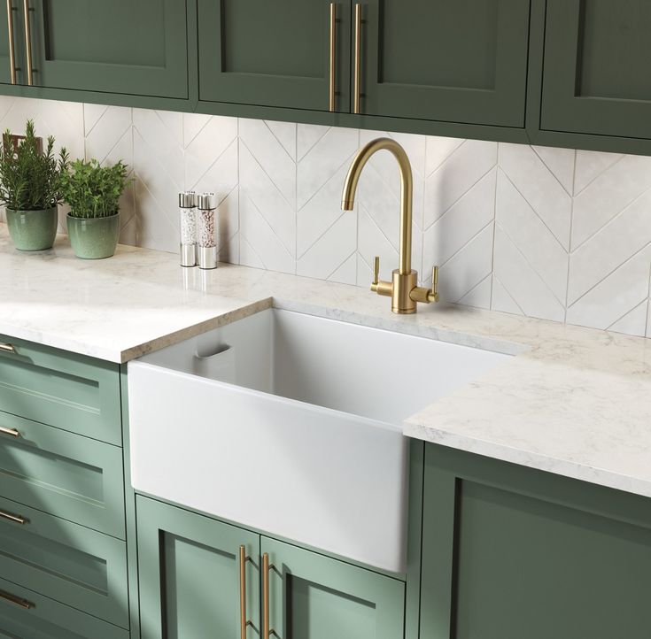 a kitchen with green cabinets and white marble counter tops, gold faucets and brass handles