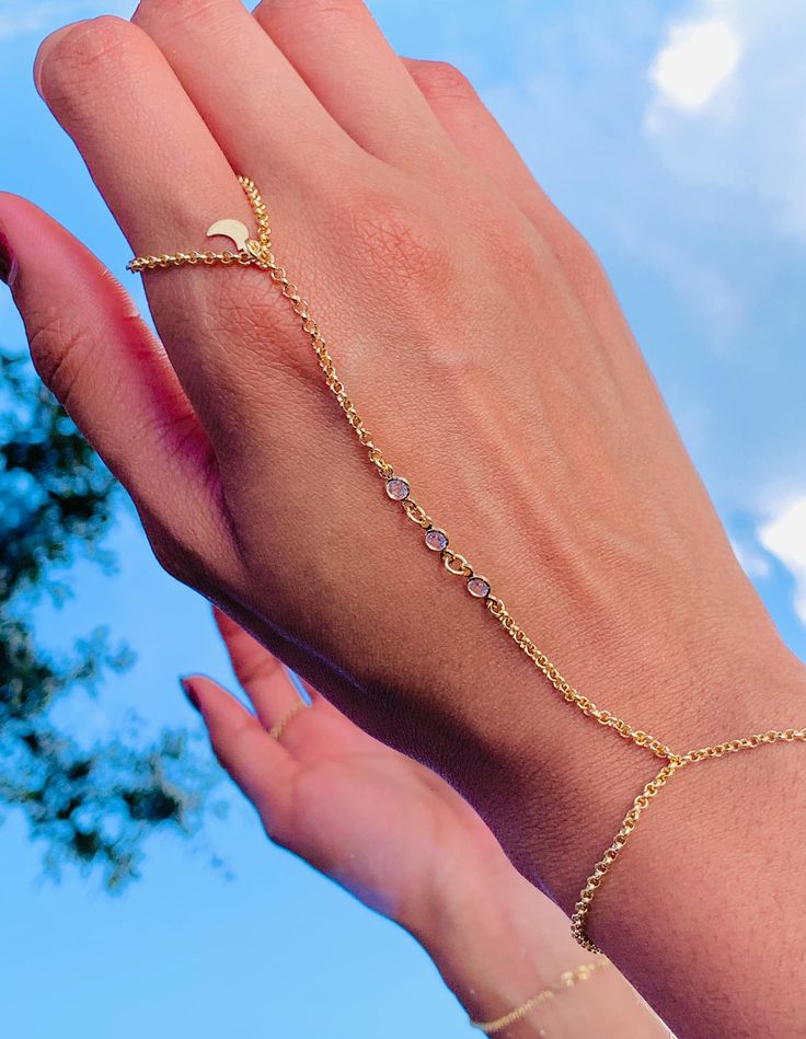 Our 18-karat gold-filled CZ hand chain with a moon charm is a beautiful and trendy piece of jewelry. This hand chain features a delicate chain that wraps around the wrist and connects to a ring, creating an elegant look. The moon charm adds a celestial touch, perfect for those who love astrology or simply appreciate the beauty of the night sky. Bracelet length:  6" + .5" Extension Finger Loop: 2.5"  Hand Chain Piece: 3.75" Material: 18 Karat Gold Filled, Hypoallergenic. Tarnish Resistant. Gold-filled does not de-laminate or peel like Gold plated Jewelry nor does it tarnish as readily as silver. Generally speaking, gold filled is better quality and will have a much longer lasting color than plated jewelry. Gold filled jewelry is an excellent option for those who wish to have a product of ex Hand Chain Bracelet, Dainty Style, Love Astrology, Ring Hand, Celestial Jewelry, Alessandra Ambrosio, Delicate Chain, Hand Chain, Vanessa Hudgens