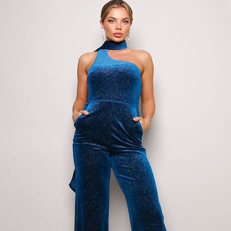 Scarf Top Glitter Velvet Jumpsuit. Sleeveless One Shoulder. Diagonal Neckline. Wrap Around Scarf Detail. Darted For A Contoured Bust. Front Side Pockets Open Back Detail. Invisible Back Zip Closure. Long Pants That Elongate The Legs. Looser Fit Toward The Bottom To Keep You Comfortable 95% Polyester 5% Spandex Glamorous Blue Sleeveless Jumpsuits And Rompers, Glamorous Sleeveless Jumpsuits For Holidays, Blue Glamorous Fitted Jumpsuits And Rompers, Blue Stretch Jumpsuits And Rompers For Party, Glamorous Blue Jumpsuits And Rompers For Party, Blue Fitted Strapless Jumpsuit For Night Out, Blue Jumpsuits And Rompers For Party Season, Chic Blue Strapless Jumpsuit For Party, Wrap Around Scarf