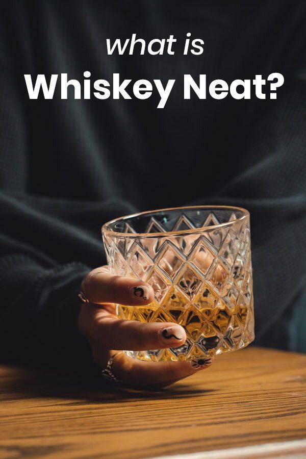 a person holding a glass on top of a wooden table with the words, what is whiskey neat?