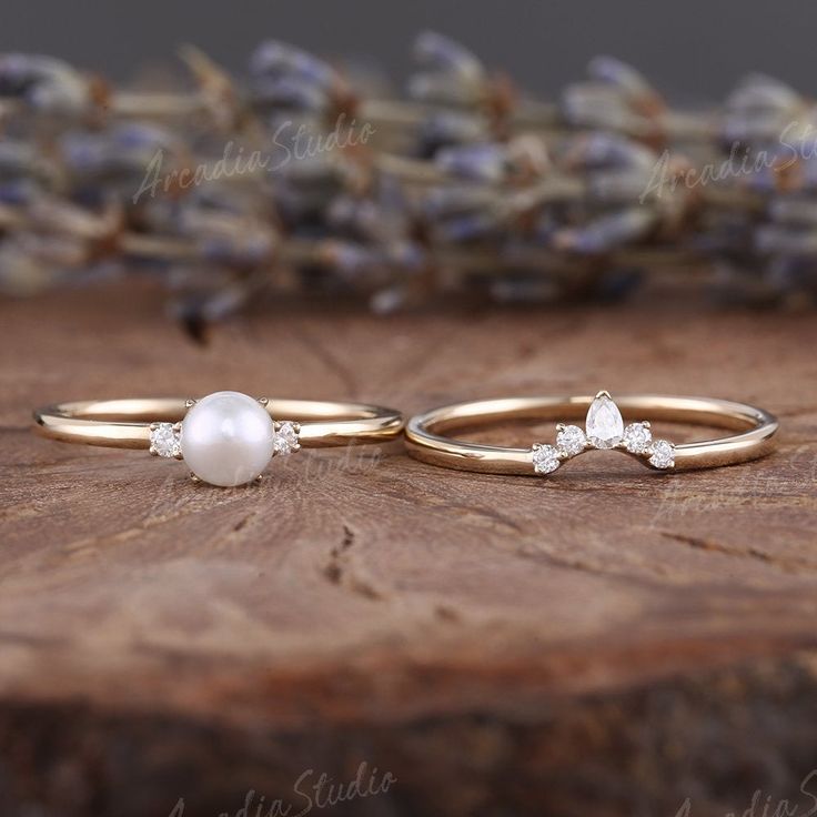 two gold rings with pearls and diamonds on a wooden table next to dried lavenders