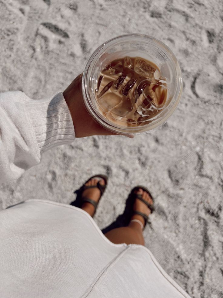 a person holding up a cup with ice and water in it's hand on the beach