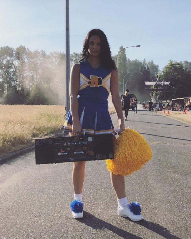 a woman in cheerleader attire holding a boombox and some pom - poms