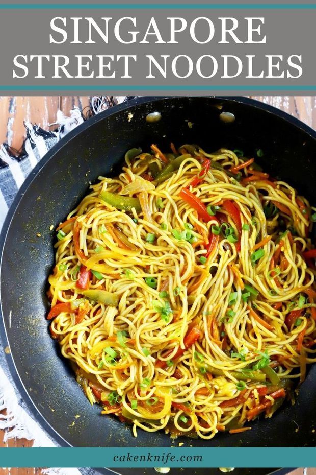 a skillet filled with noodles and vegetables on top of a wooden table next to a plate