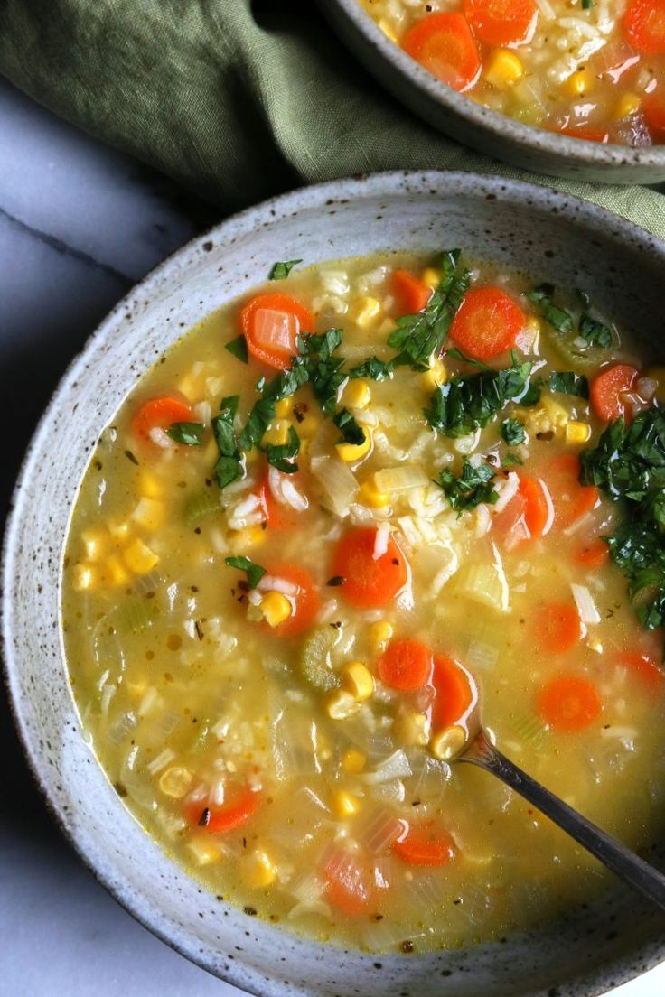 two bowls of soup with carrots, corn and spinach on the top one has a spoon in it