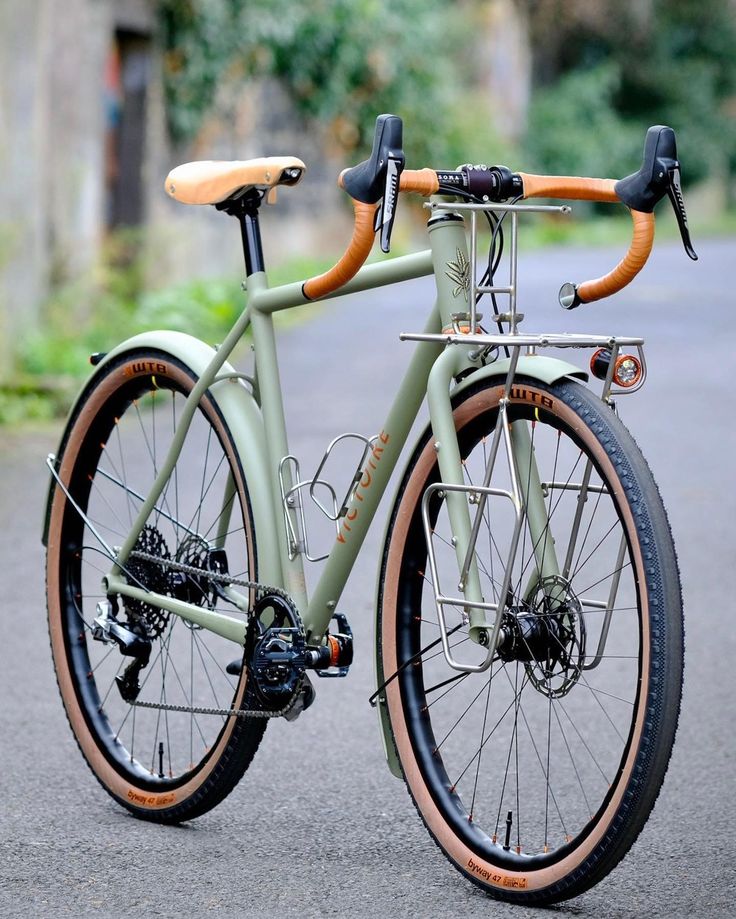 a green bike with wooden spokes parked on the side of a road in front of some trees