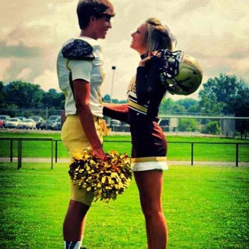 a man and woman standing on top of a lush green field holding cheerleader's pom poms