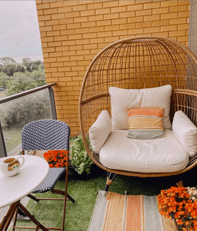 a wicker swing chair and table on a balcony with flowers in the foreground