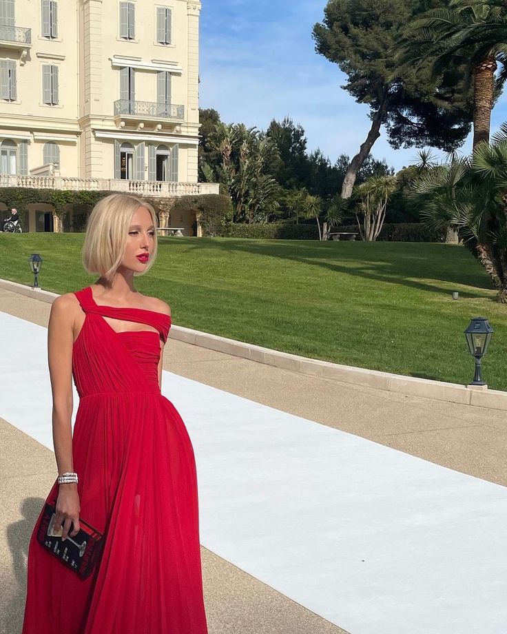 a woman in a red dress is standing on the sidewalk near a large white building