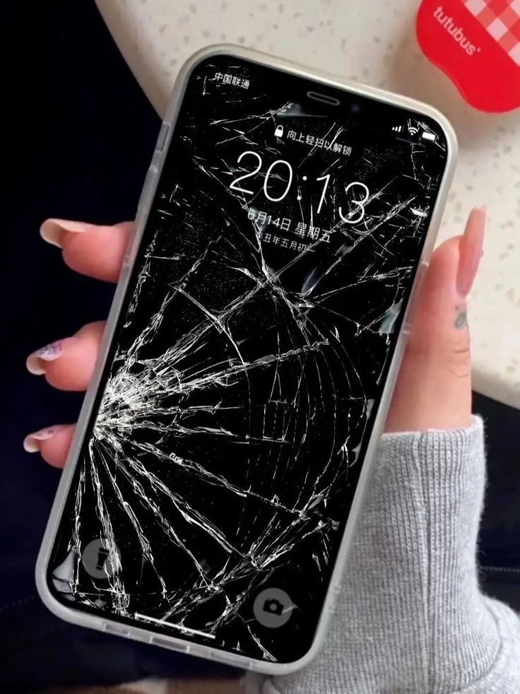 a woman holding up her cell phone with the cracked screen