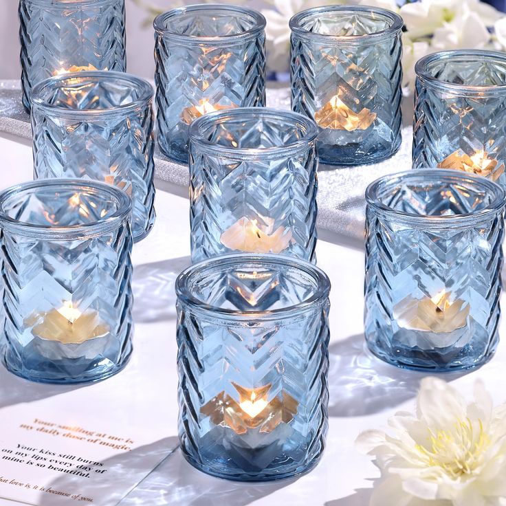 many blue glass candles are sitting on a table with white flowers in the back ground