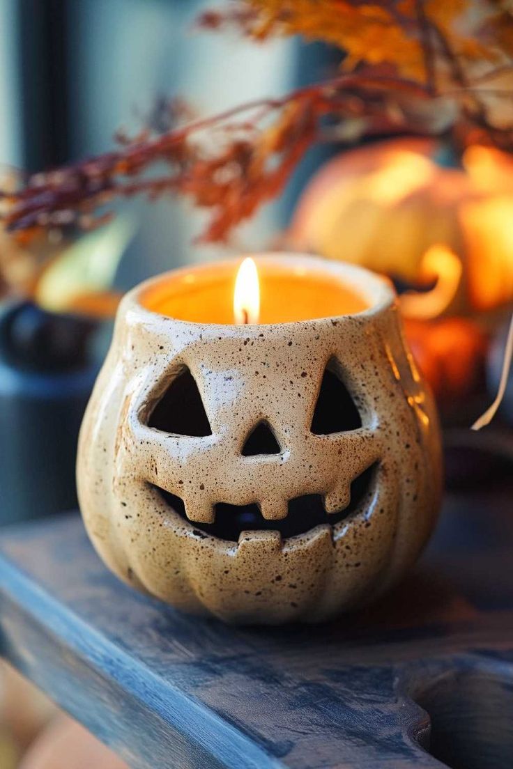 a candle that is sitting on a table with some pumpkins in the back ground