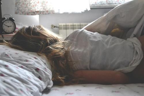 a woman laying in bed with an alarm clock on the nightstand next to her head