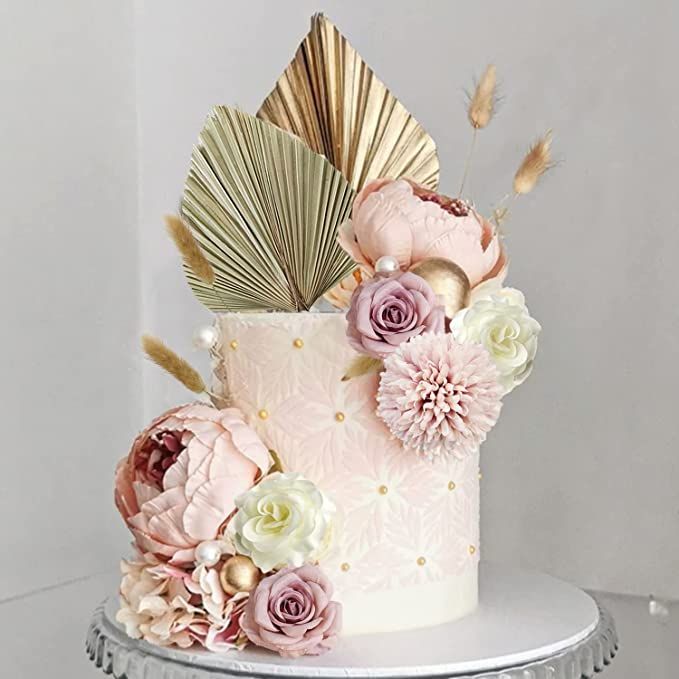 a white cake with pink flowers and gold leaves on top, sitting on a silver platter