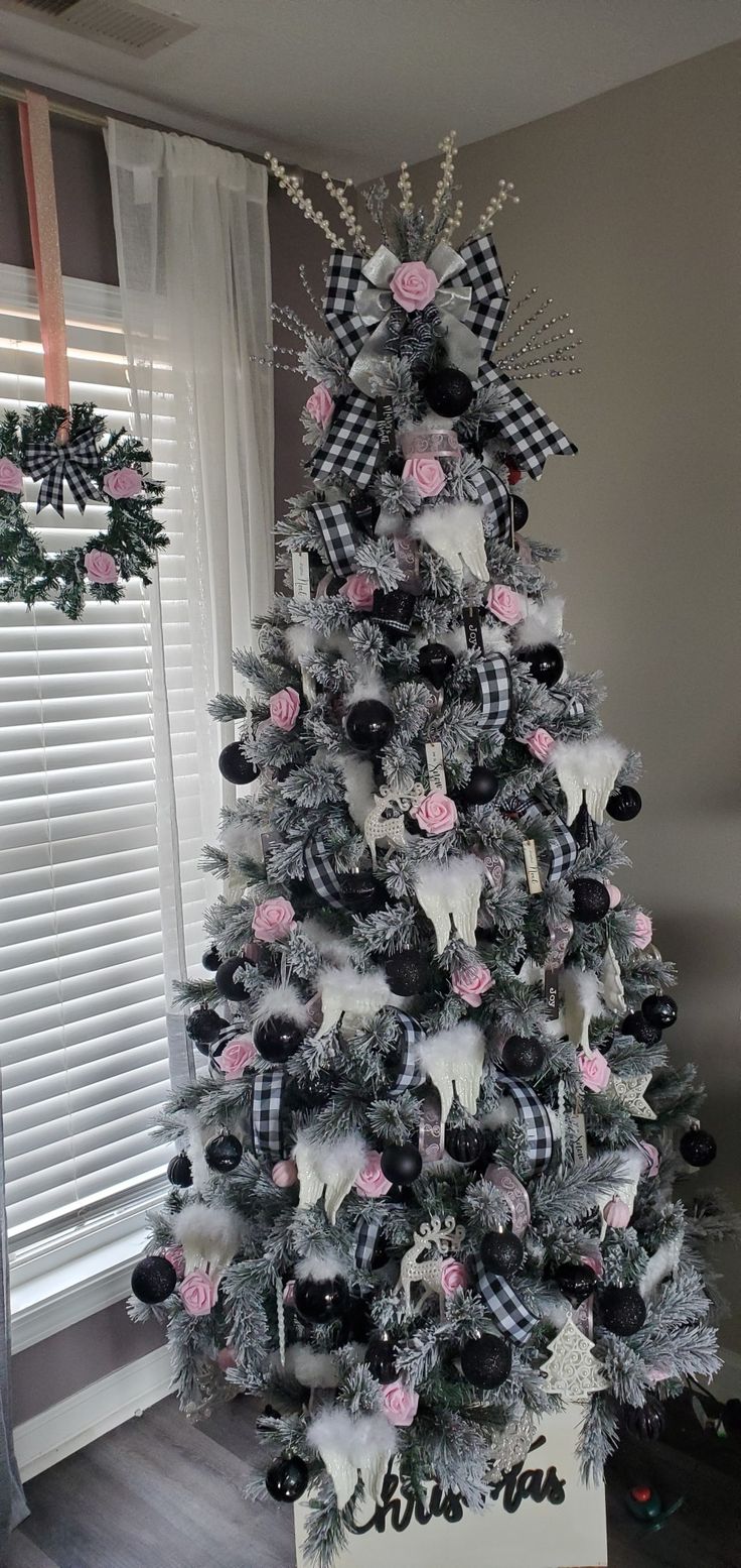 a christmas tree decorated with black, white and pink ornaments is in front of a window