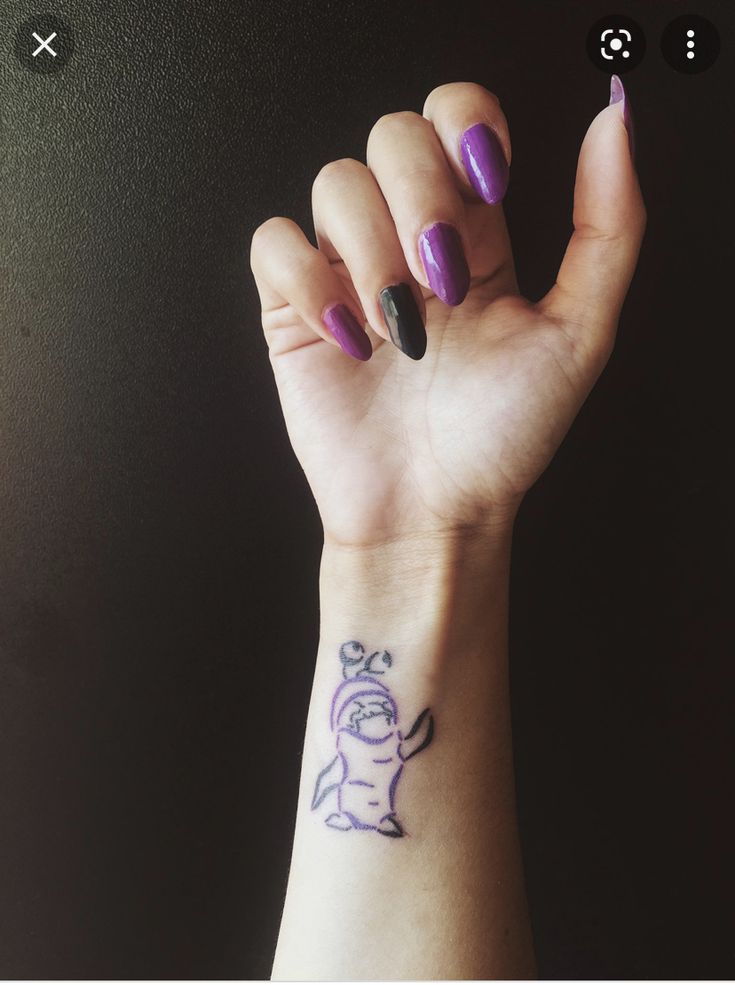 a woman's hand with purple and black nail polish holding up her wrist tattoo