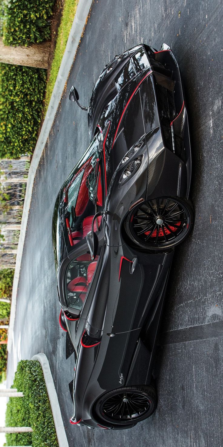 a black sports car parked on the side of a road next to a hedge covered wall