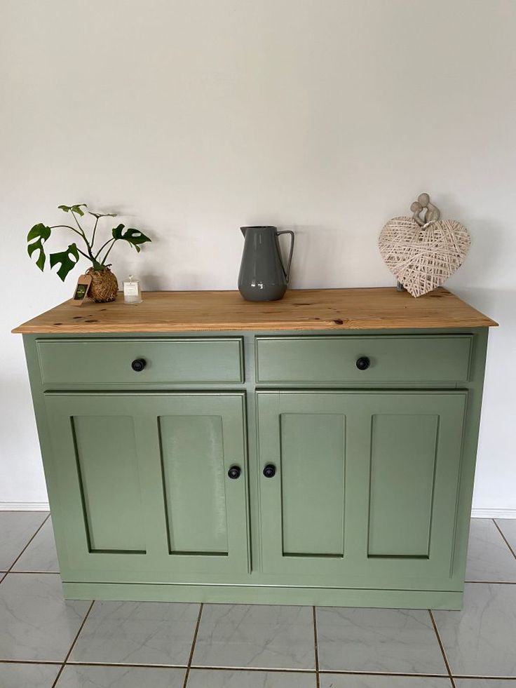 a green cabinet sitting on top of a tiled floor next to a vase and potted plant