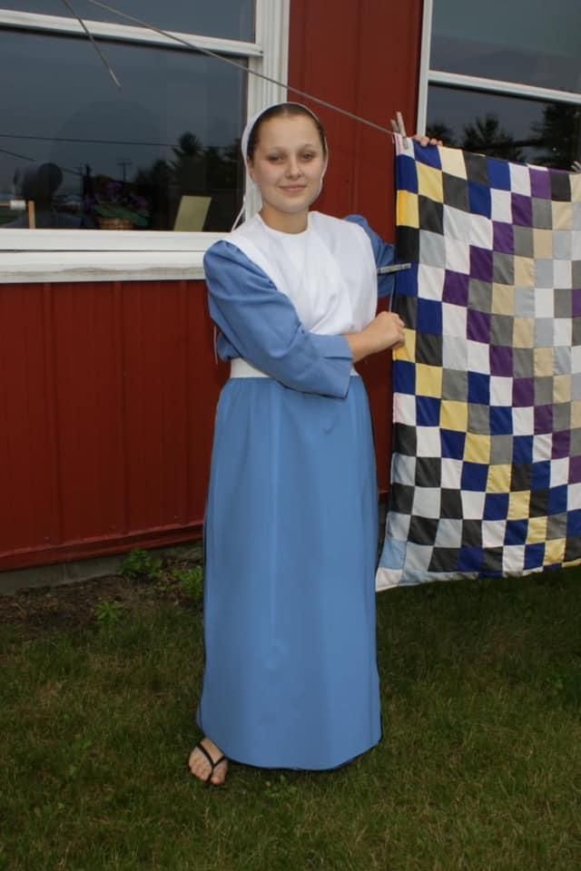 a woman standing next to a quilt on a clothes line