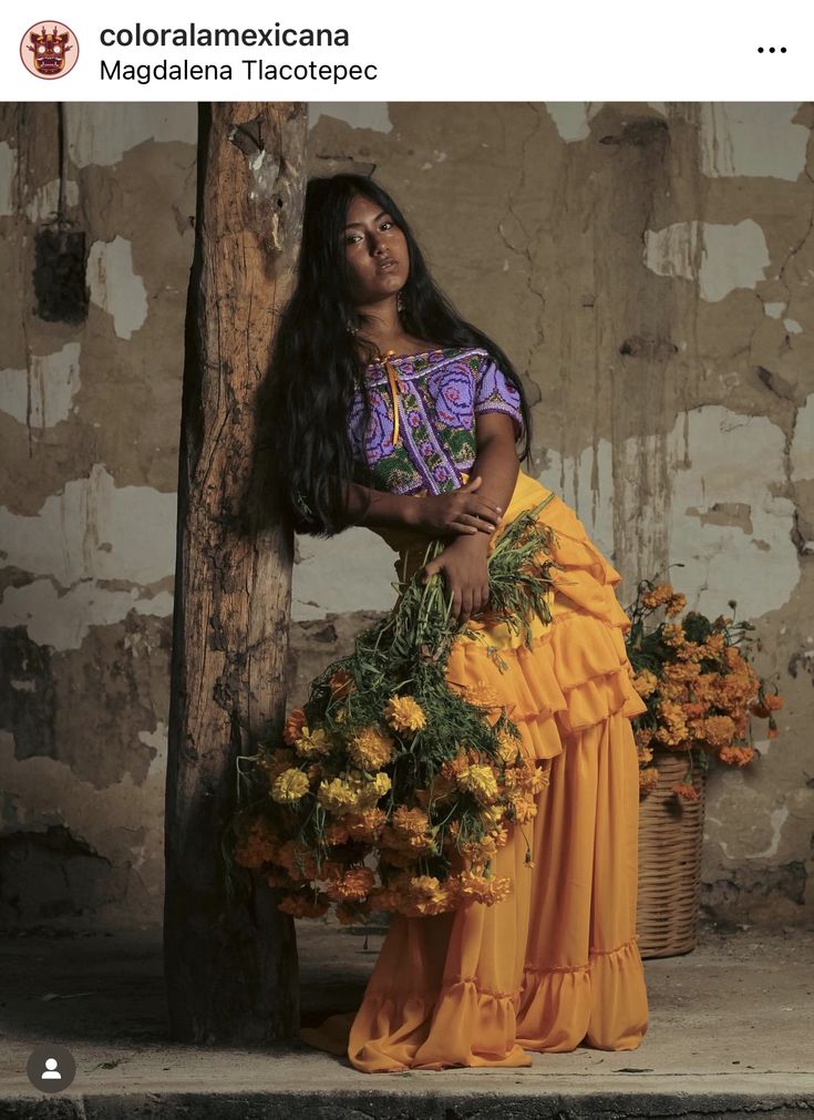 a woman with long black hair is sitting on a wooden pole holding yellow flowers in her hands