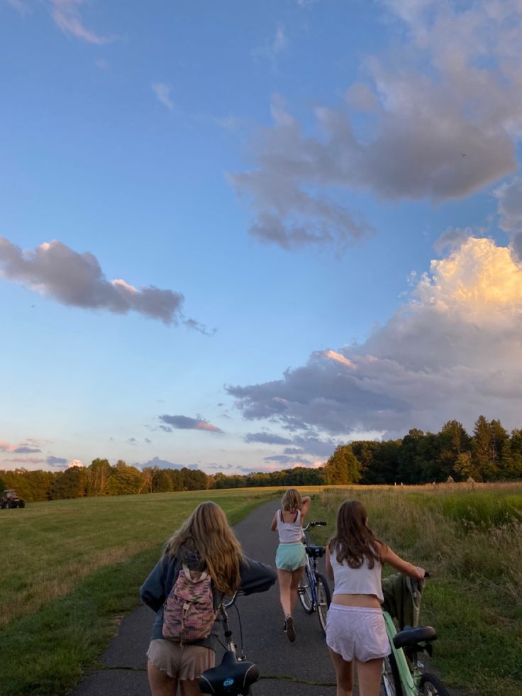 two girls are walking down the road with their bikes and one girl is pushing her stroller