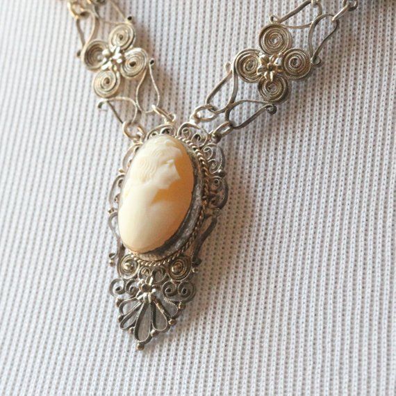 Featured in this listing is a beautiful vintage cameo necklace. The silver tone metal has been hand wrapped to make unique curls and design. Three oval cameos are bezel set. The center cameo is 20x15.6mm and the two smaller cameos are 16.2x12.6mm. The center piece is connect with chain. The necklace lays nicely on the chest for a lovely vintage look.Size: 21 inches longCondition: very good vintage conditionOriginality: silver toneWeight: 9.5dwt, 14.7gRef: 540-10153===============►YourPersonalGol Handmade Silver Jewelry For Vintage Events, Collectible Art Nouveau Carved Jewelry, Ornate Cameo Jewelry For Formal Occasions, Ornate Antique Silver Carved Jewelry, Victorian Carved Silver Jewelry, Victorian Style Carved Silver Jewelry, Handmade Silver Necklaces For Vintage Events, Handmade Silver Necklaces For Vintage Occasions, Ornate Cameo Jewelry For Vintage Events