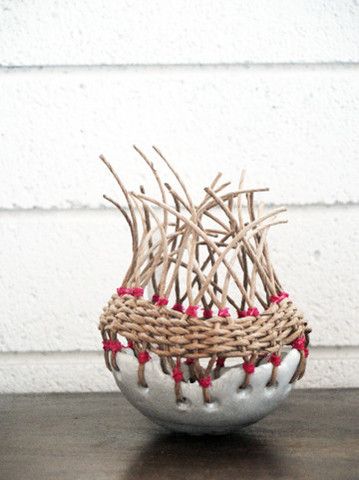 a bowl with sticks sticking out of it on top of a wooden table next to a white wall