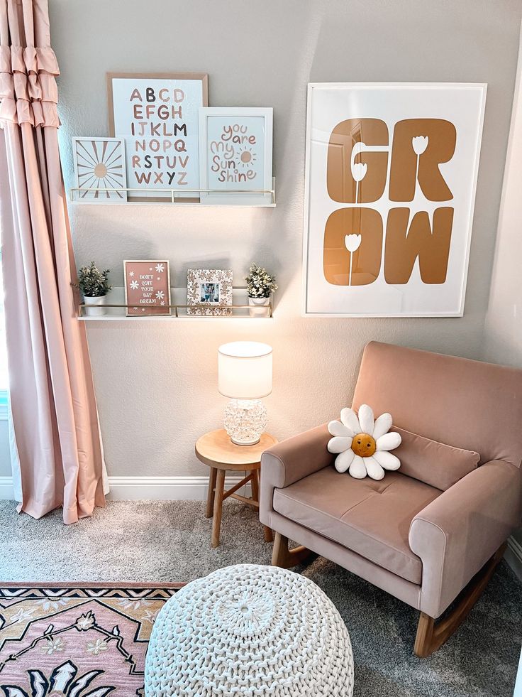 a chair and ottoman in a small room with pink curtains, pictures on the wall