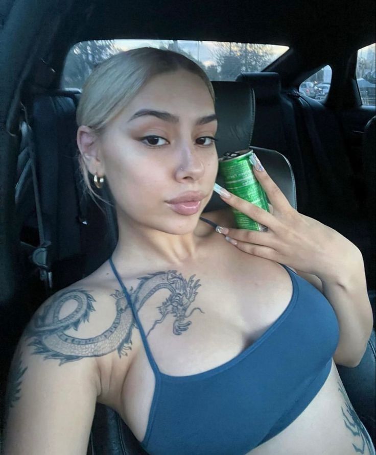 a woman sitting in the back seat of a car holding a can of beer and looking at her cell phone