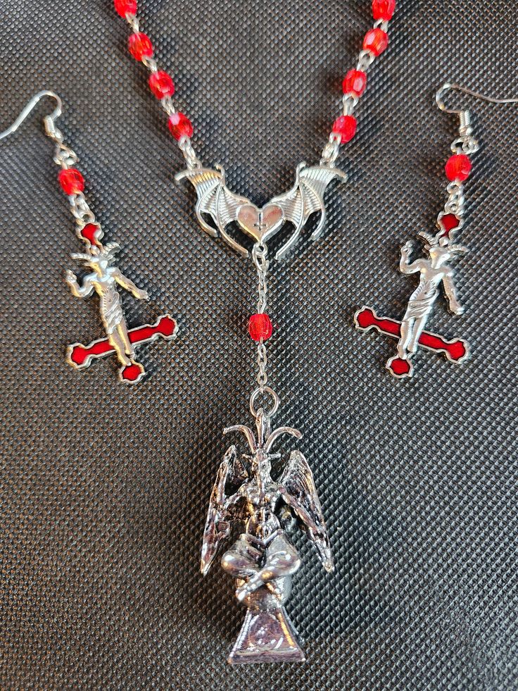 Vintage Red Pope Rosary Upcycled w/ Baphomet Pendant, Wing Center & Matching Inverted Cross Baphomet Earrings  This stunning upcycled vintage Pope John Paul II anniversary rosary features a gorgeous Baphomet pendant, bat wing & inverted cross centerpiece, original Pope coin connector pieces at top of piece & matching inverted cross Baphomet earrings. This is a one of a kind necklace that is an ultimate conversation piece that's fiercely fashionable as well. Necklace dimensions: 12.5" x 1.5" Earring dimensions: 3" x 1" Weight: 1.75 oz Forsaken Creations was founded in early 2023 with a passion for upcycling broken and vintage jewelry, namely rosaries, in various alternative style fashions. All items are hand crafted/altered by me in order to make the most interestingly different, fashionabl Handmade Gothic Horned Jewelry, Adjustable Red Gothic Jewelry, Red Punk Jewelry For Festival, Adjustable Red Fantasy Jewelry, Red Fantasy Metal Jewelry, Fantasy Red Metal Jewelry, Handmade Red Punk Jewelry, Handmade Punk Red Jewelry, Red Fantasy Jewelry For Halloween