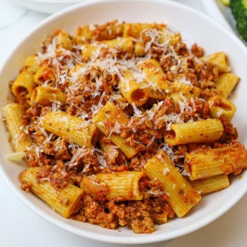 a white bowl filled with pasta covered in sauce and parmesan cheese on top