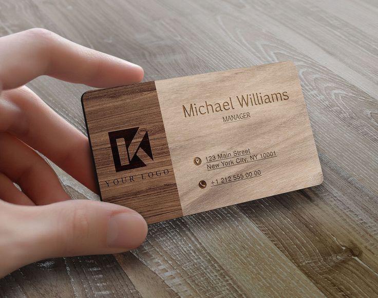 a hand holding a wooden business card on top of a table with wood grained flooring