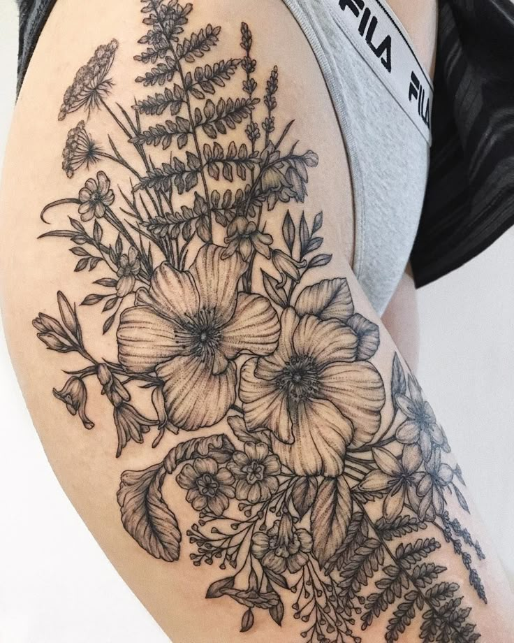 a woman's thigh with flowers and leaves on the back of her leg, which is covered in black ink