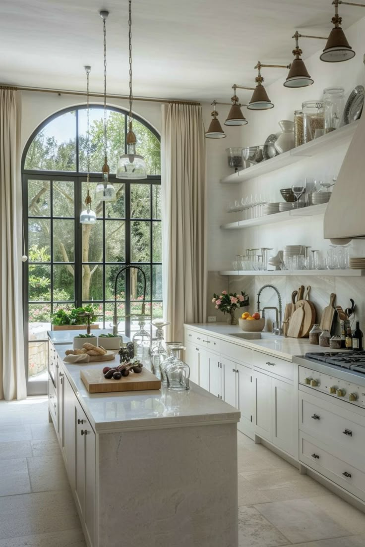 a large kitchen with lots of white cabinets and open shelves on the wall, along with an arched window