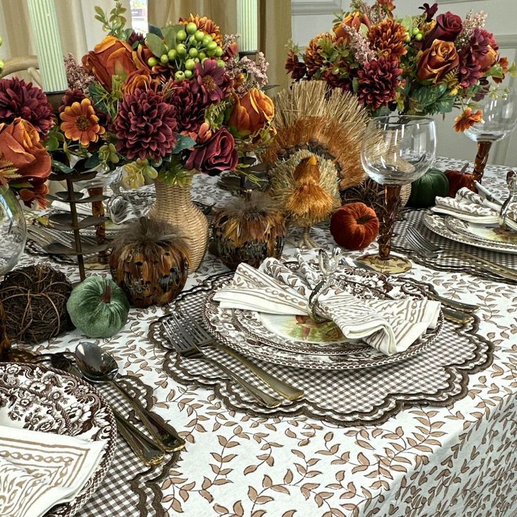 the table is set with plates, silverware and vases filled with autumn flowers