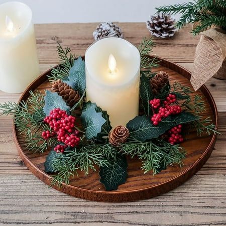 two candles are sitting on a wooden plate with holly and pine cones, red berries, and evergreen leaves