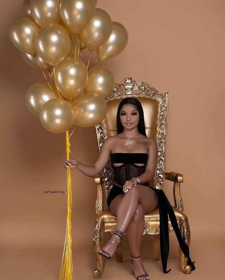 a woman sitting on a gold chair with balloons in the air above her head,