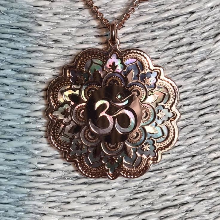 "Om in rose gold on 925 silver and black mother of pearl backdrop. Om is one of the most important spiritual symbols, a sacred sound in Indian religions, found also in some chapters of the Veda. It has variously been associated with concepts of \"cosmic sound\" that celebrates the creative powers of the Universe. Its sound is made up of three syllabes (A-U-M): wakefulness / darkness / present, dream / unconscious / past, deep sleep / future truth. In the jewel The five curves shaping the Om symb Spiritual Rose Gold Jewelry For Meditation, Engraved Rose Gold Spiritual Necklace, Spiritual Rose Gold Copper Necklace, Spiritual Rose Gold Medallion Jewelry, Rose Gold Jewelry For Festivals Gift, Rose Gold Jewelry For Festivals And Gifts, Festive Rose Gold Jewelry Gift, Spiritual Copper Jewelry For Meditation, Spiritual Copper Medallion Necklace