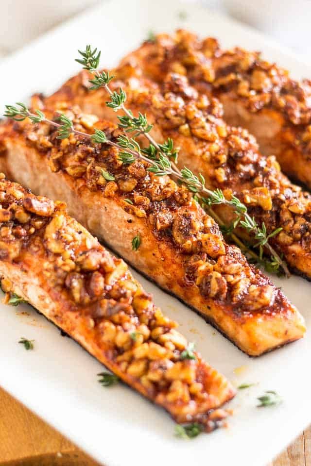 grilled salmon fillets on a white plate topped with fresh herbs and seasoning