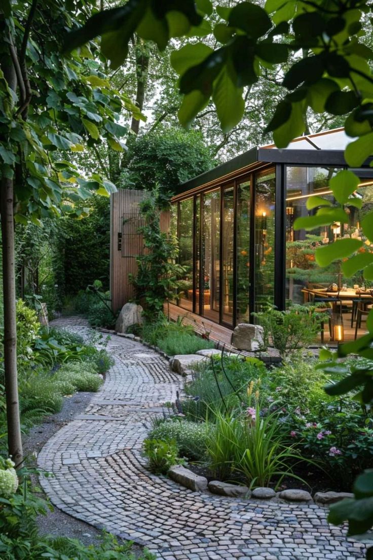 a brick path leads to a glass - walled building in the middle of a garden