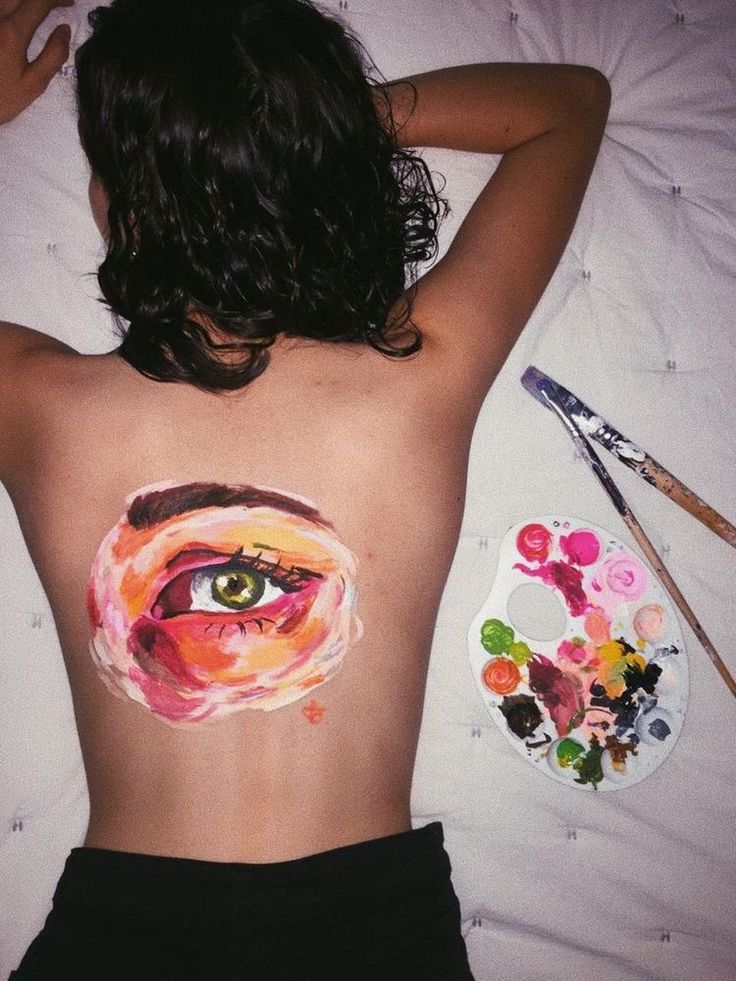 a woman laying on top of a bed with her back turned to the camera and an eye painted on her stomach