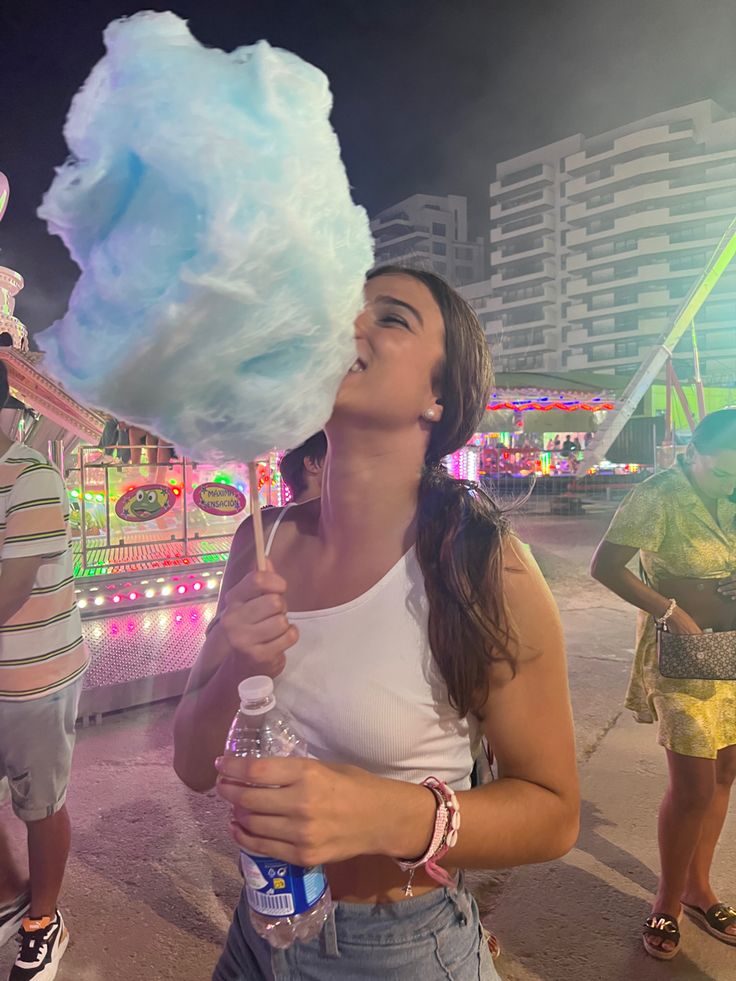 a woman holding a giant cotton candy lollipop in front of some carnival rides