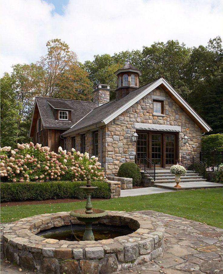 a stone house with a fountain in the front yard and flowers on the back lawn