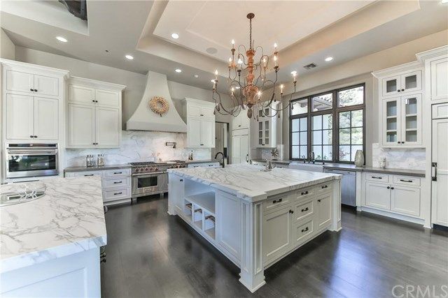 a large kitchen with marble counter tops and white cabinets, along with a chandelier hanging from the ceiling