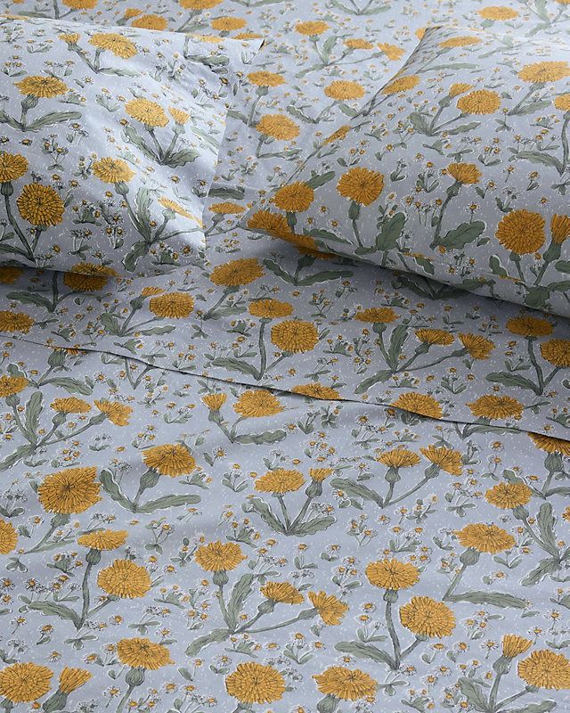 a bed with yellow flowers and green leaves on it's coverlet, next to a pillow