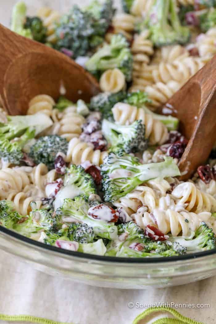 pasta salad with broccoli and cranberries in a glass bowl, topped with wooden spoons