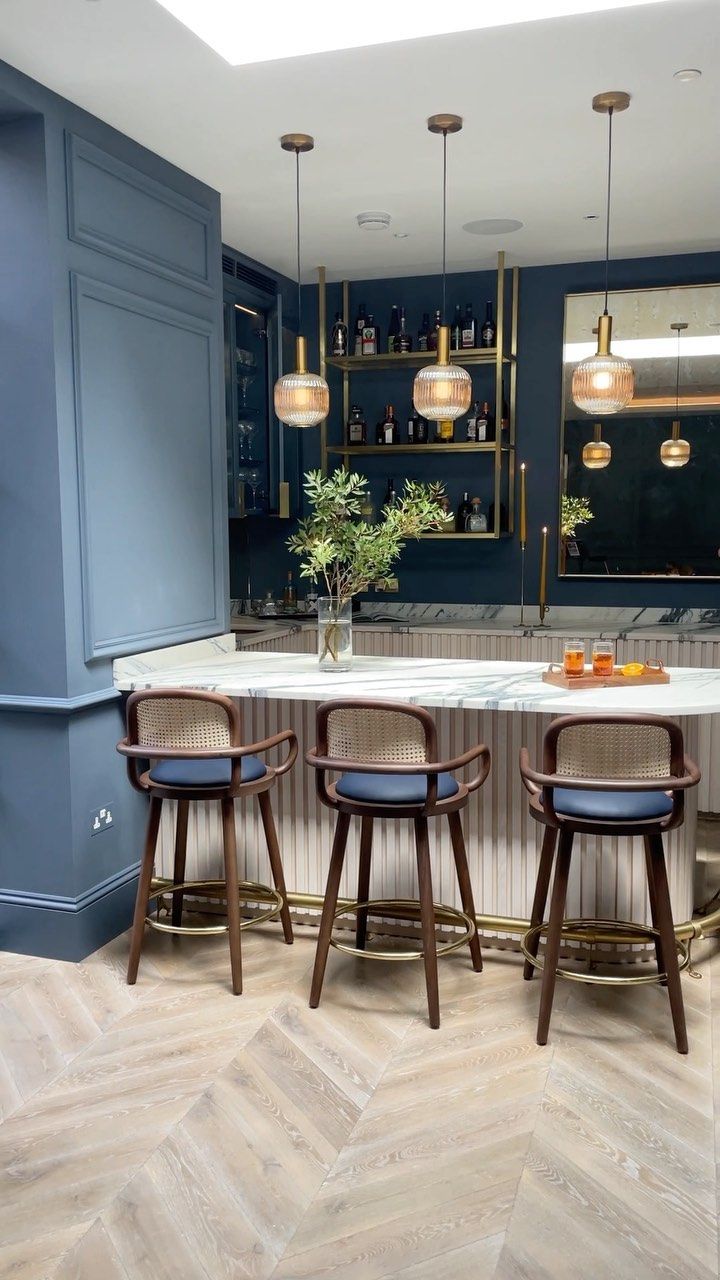 a kitchen with blue walls and wooden stools at the bar area, along with marble counter tops