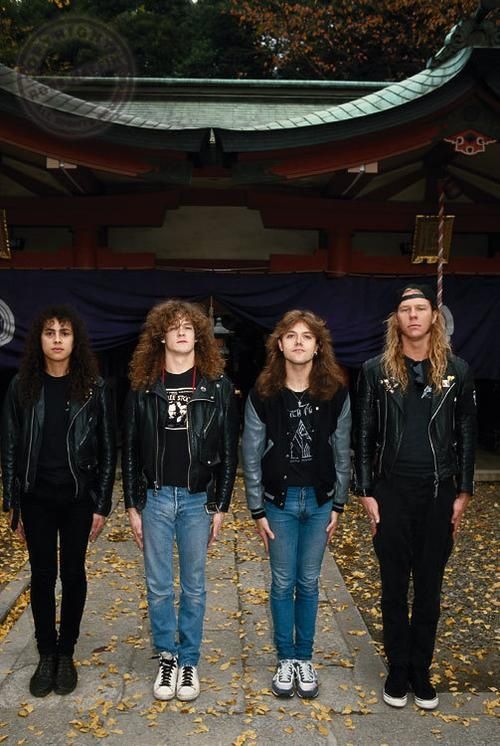 four people standing in front of a building with trees and leaves on the ground behind them