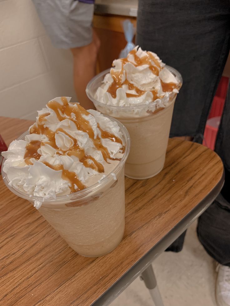 two cups with whipped cream and caramel toppings sitting on top of a table