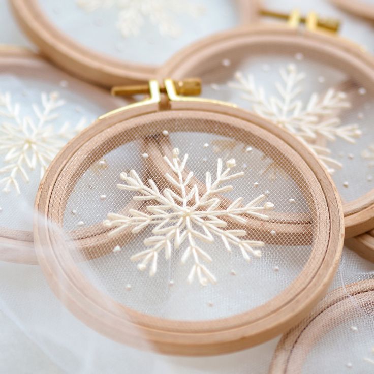 several embroidery hoop with snowflakes on them sitting next to each other in front of white fabric